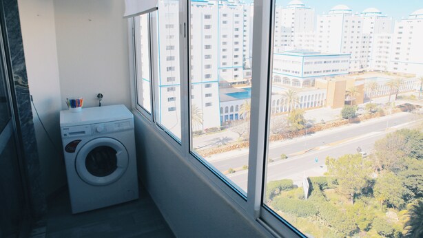 A laundry room with a washing machine, large windows, and a view of high-rise buildings. - Algarve Panorama Holidays (Portimão)