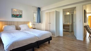 A bedroom with a double bed, a bedside table, a nightstand, a wardrobe, and a bathroom visible through an open door. - Terrace Stay near Shoreline (Berck-Sur-Mer)