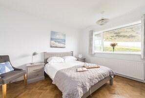 A bedroom with a bed, bedside table, lamp, chair, and a window with a view.