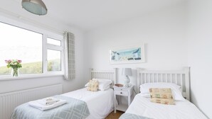 Een slaapkamer met twee bedden, een nachtkastje, een lamp, een raam met uitzicht en een schilderij aan de muur.