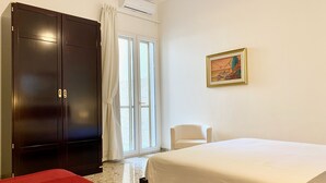 Hotellihuone, jossa on suuri vaatekaappi, sänky, tuoli ja taulu seinällä.