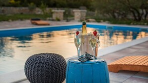 A poolside setting with a champagne bottle and glasses, a knitted stool, and a wooden bench. - Villa Red Hacienda with Pool (Vodice)