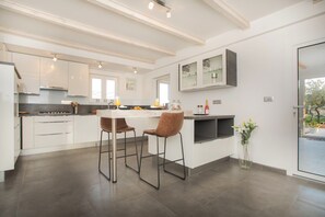 Una cocina moderna con armarios blancos, una isla central, dos taburetes de bar y una mesa de comedor.