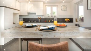 A modern kitchen with a central island, two bar stools, and a dining table set for two. - Villa Red Hacienda with Pool (Vodice)