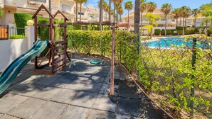A playground with a slide and swing set, a swimming pool, and a view of residential buildings.