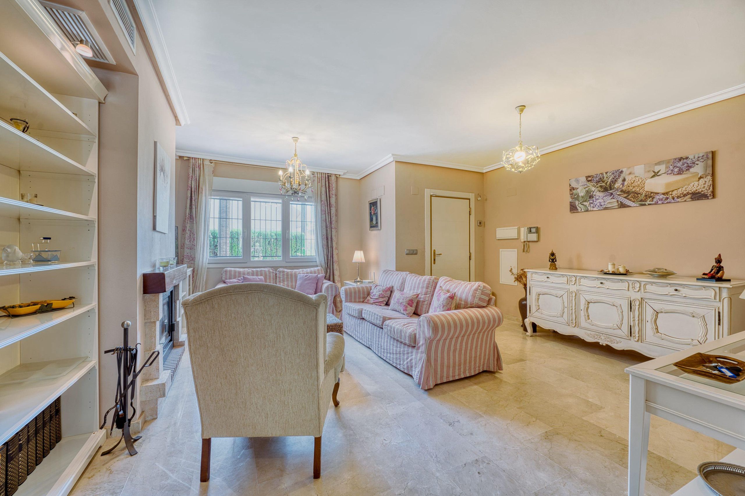 A spacious living room with a fireplace, a sofa set, a dining area with a white cabinet, and a chandelier.