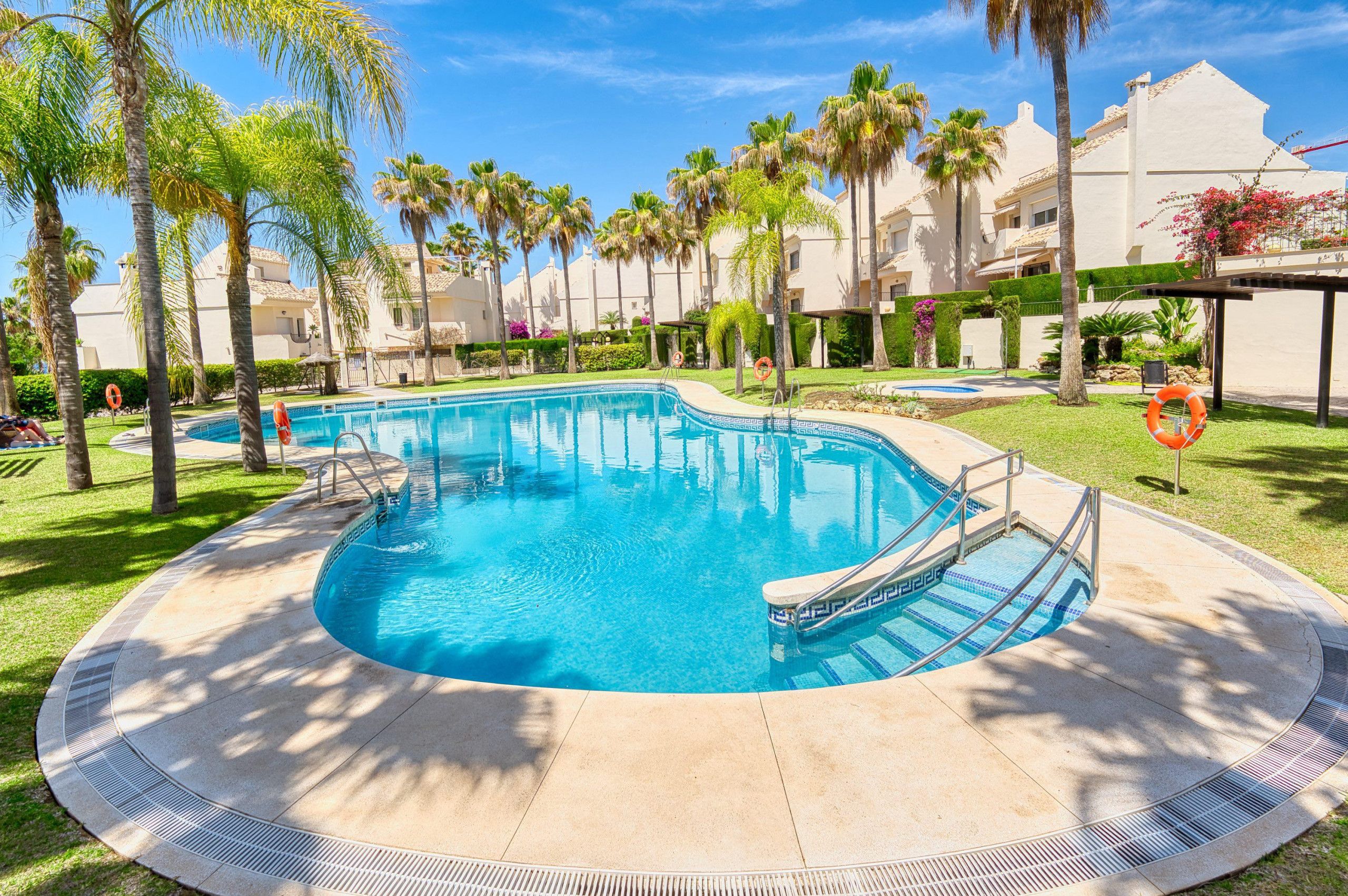 A swimming pool surrounded by palm trees and a building with a white facade.