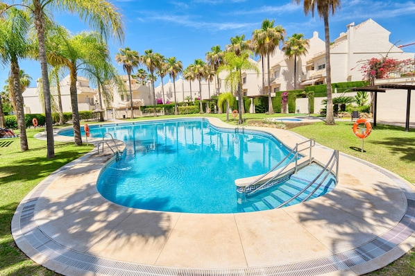 A swimming pool surrounded by palm trees and a building with a white facade.