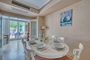 Uma sala de jantar com uma mesa redonda posta para quatro pessoas, cadeiras brancas e um quadro na parede.