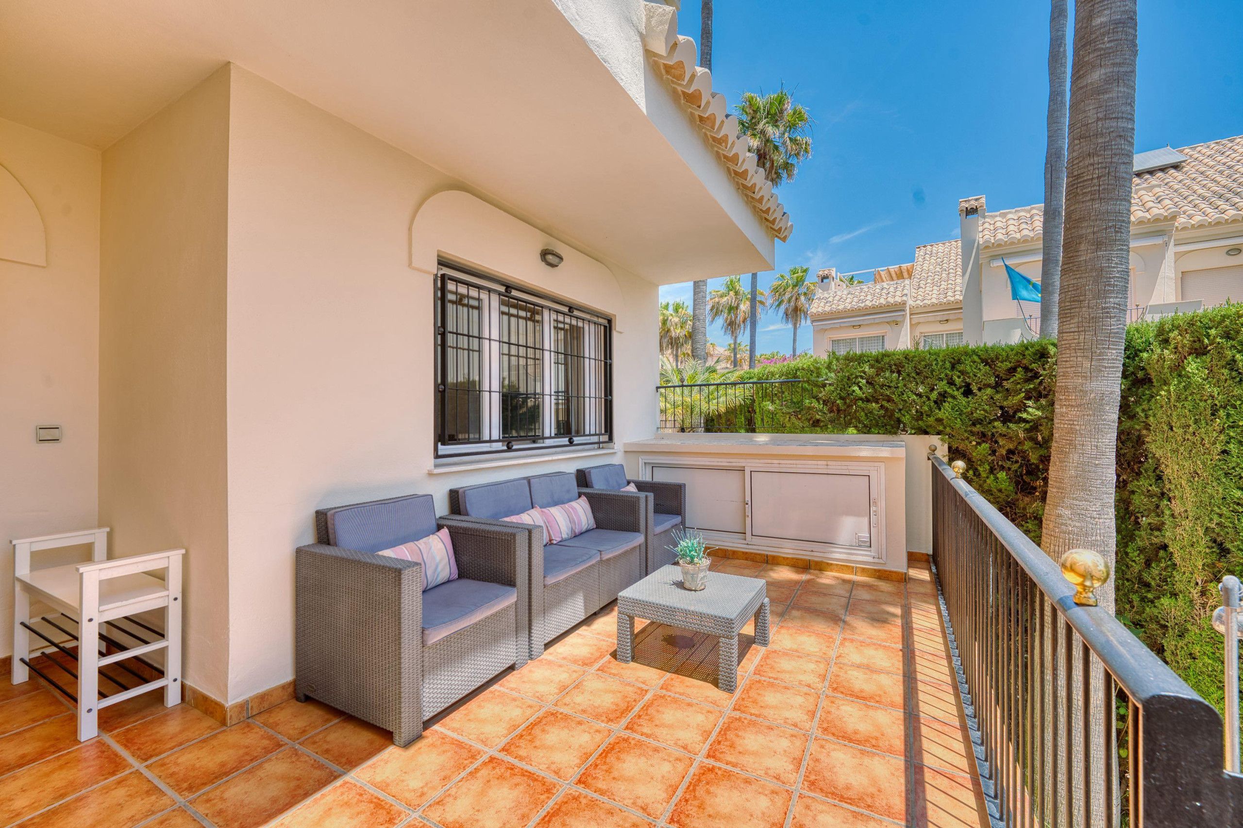 A balcony with wicker furniture, a small table, and a window with bars.