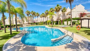 A swimming pool surrounded by palm trees and a building with a white facade.