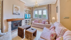 A living room with a fireplace, striped sofas, wicker ottomans, and a television.