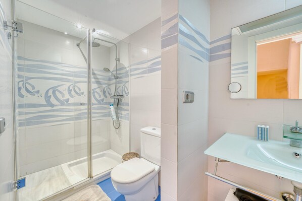 Une salle de bain moderne avec une douche à parois de verre, des toilettes blanches et un lavabo en verre avec un miroir au-dessus.