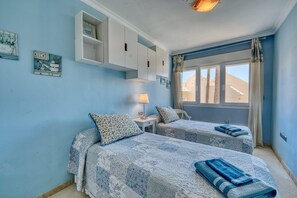 Une chambre avec deux lits, une table de chevet, une lampe et une fenêtre avec des rideaux.