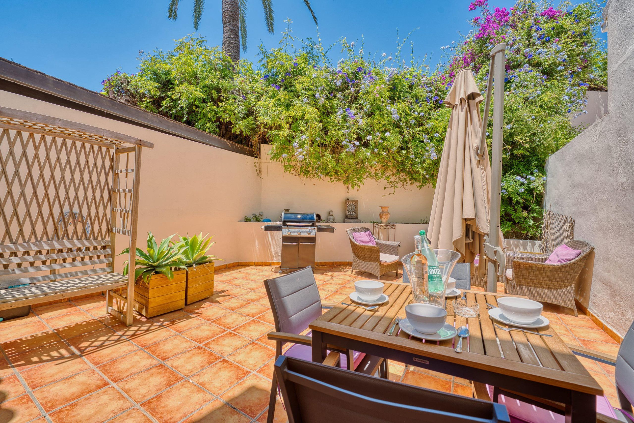 A patio with a dining table, chairs, a grill, and a seating area with a wooden lattice.