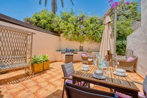 Une terrasse extérieure avec une table en bois, des chaises, un barbecue et des plantes en pot.