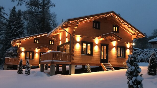 Una cabaña de madera con un porche cubierto, rodeada de árboles cubiertos de nieve.