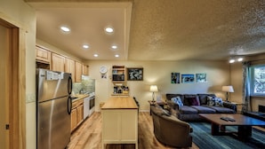 A compact kitchen with a refrigerator, stove, and microwave. There is a dining area with a table and chairs, and a living room with a sofa and a coffee table. - Hi Country Haus Unit 1503 Ground floor 1 bedroom next to the Fraser River (Winter Park)