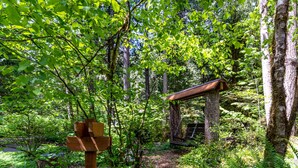 A forested area with a wooden signpost, a small wooden structure, and a moss-covered rock. - Swimming pool, pickleball, tennis, basketball courts, private hot  tub, sauna. (Glacier)