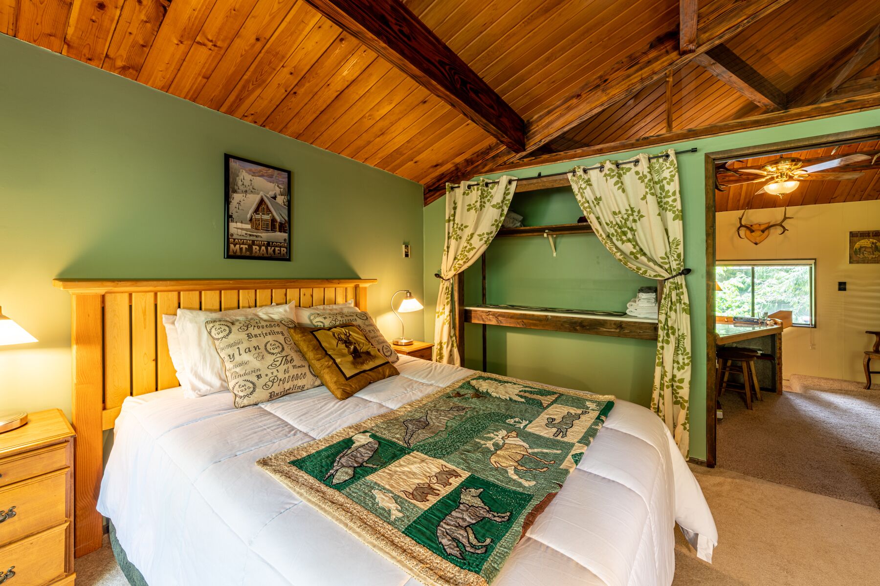 A cozy room with a wooden ceiling, a bed with a quilted blanket, a nightstand, and a window with curtains.
