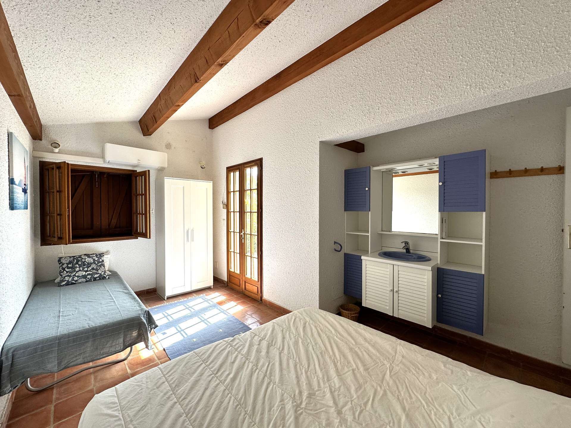 A bedroom with a bed, a wardrobe, a window, and a bathroom with a sink and mirror.