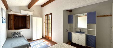 A bedroom with a bed, a wardrobe, a window, and a bathroom with a sink and mirror.