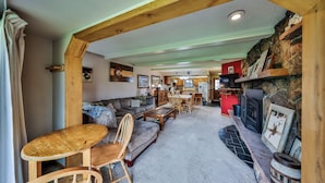 Un salon chaleureux avec une cheminée, des meubles en bois et une cuisine en arrière-plan.
