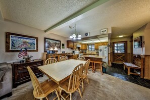 Een ruime keuken met houten kastjes, een eethoek met een grote tafel en stoelen, en een woonkamer met een bank en salontafel.