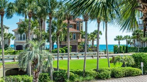 A beachfront property with a large house, palm trees, and a clear view of the ocean. - Destiny Beach Villas 15A – Lake & Gulf Views, Steps to Beach, Sleeps 6 (Destin)