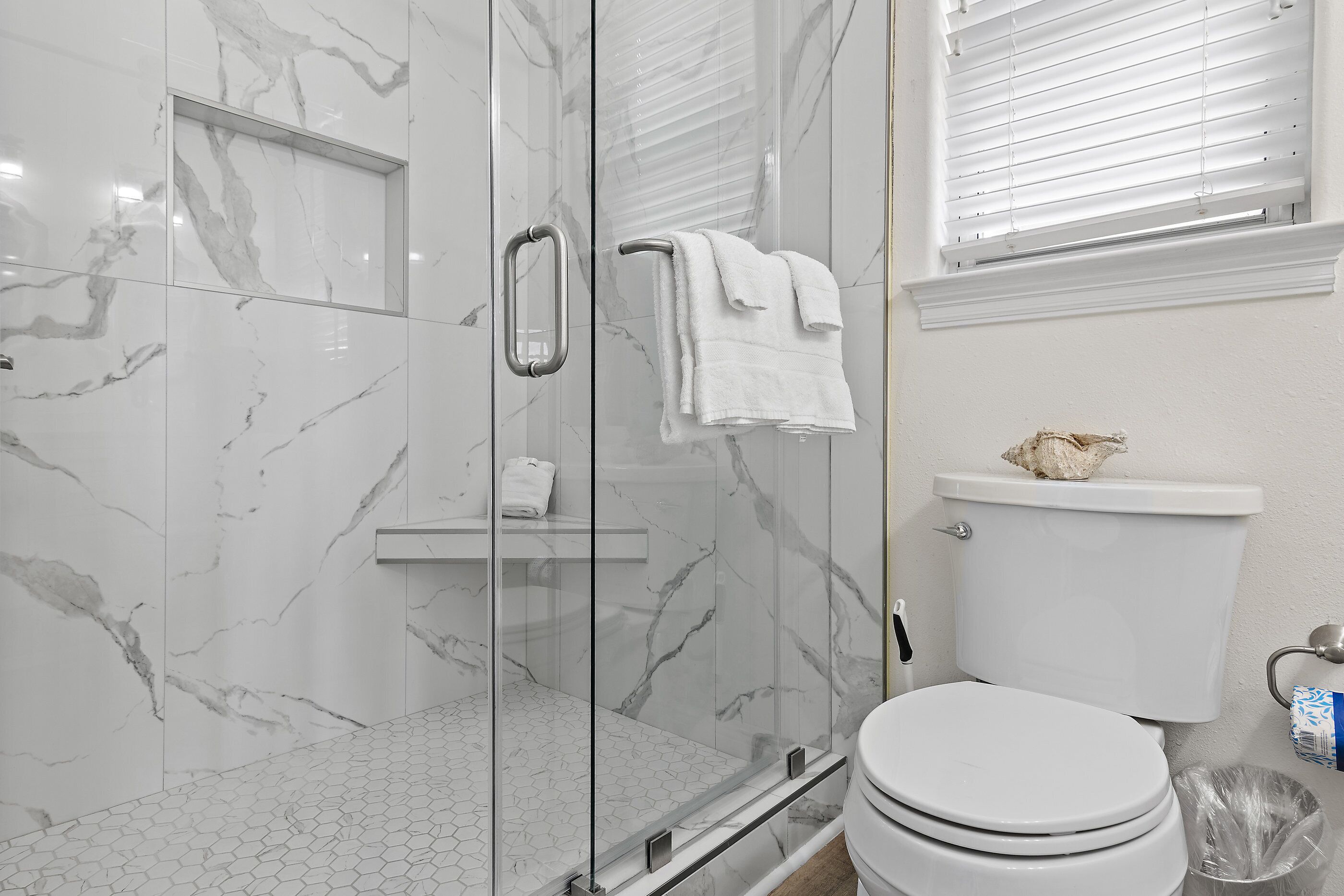 A bathroom with a glass shower enclosure, a toilet, and a sink.