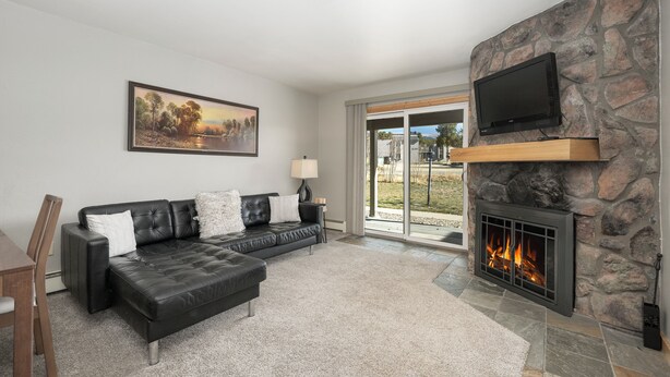 A living room with a black leather sofa, a fireplace, a television mounted on a stone wall, and a painting on the wall.