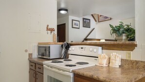 Een keuken met een magnetron, fornuis, oven, granieten aanrecht, houten kastjes en een potplant.