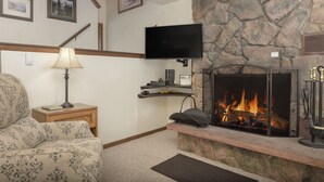 Een woonkamer met een open haard, een flatscreen-televisie aan de muur, een bank, een lamp en een accentmuur van steen.