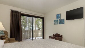 Hotelkamer met een groot bed, een aan de muur bevestigde televisie en een balkon met uitzicht op bomen.