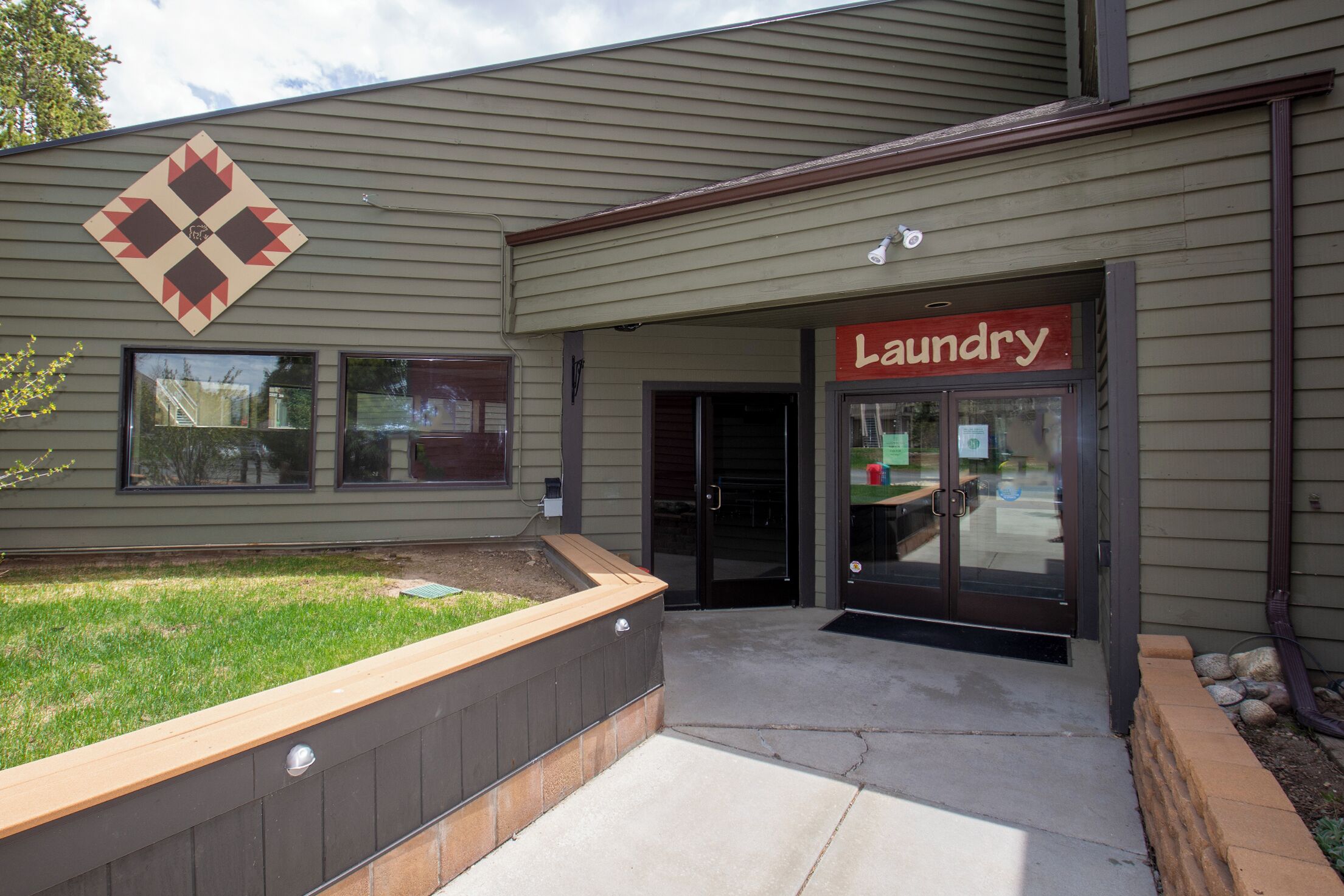 A building with a laundry facility, a landscaped area with a wooden bench, and a diamond-shaped sign above the entrance.