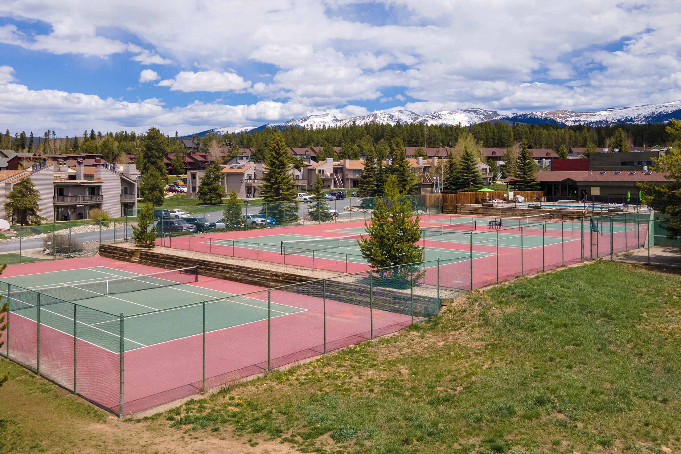 Tennis courts surrounded by mountain views and residential community in a scenic alpine setting.