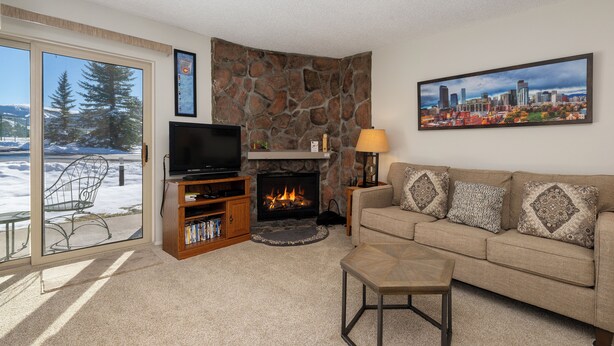 A living room with a stone fireplace, a television, a sofa with patterned cushions, and a large window overlooking a snowy landscape.
