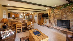 A spacious living room with a fireplace, a dining area, and a kitchen in the background.
