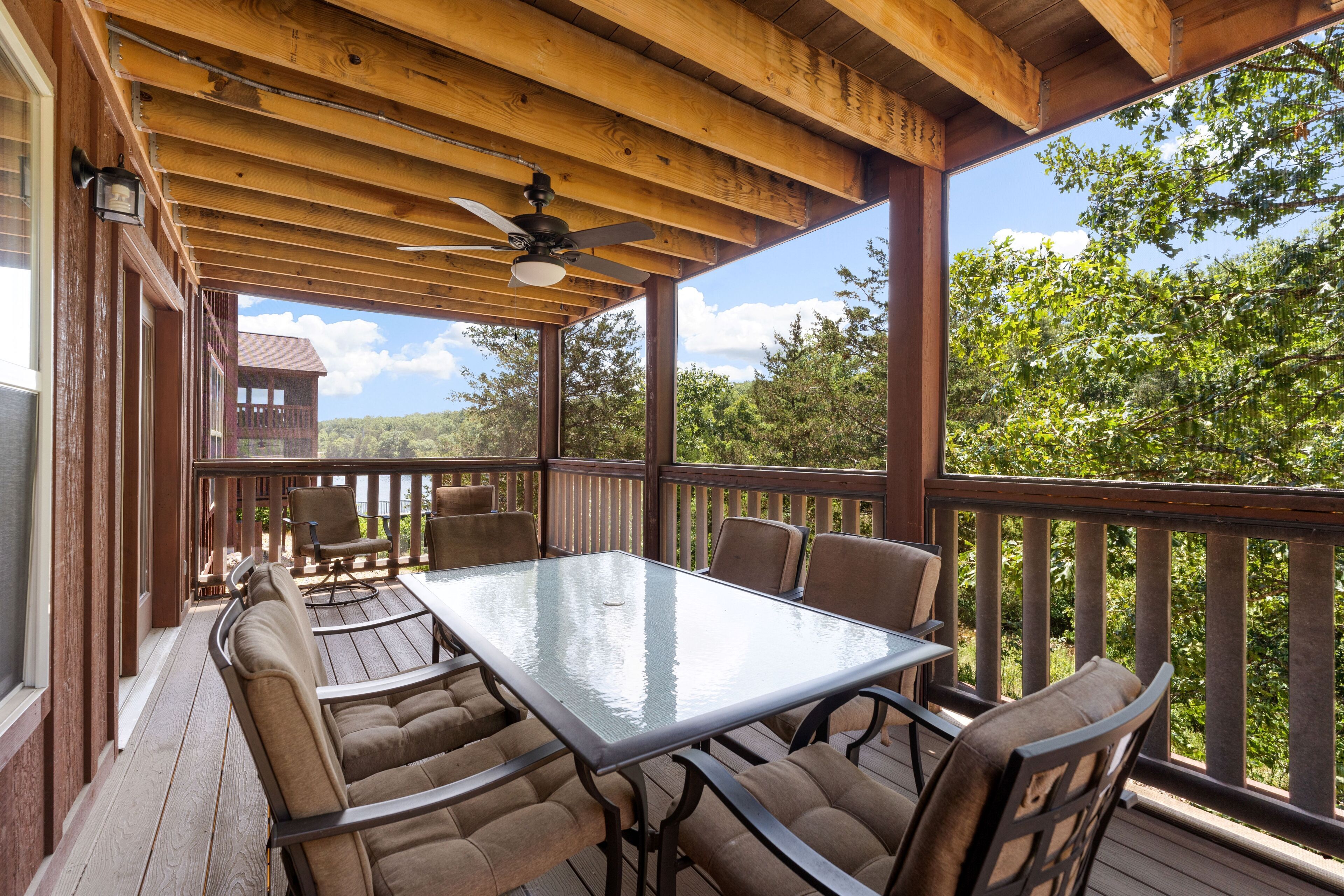 Une terrasse extérieure avec une table et des chaises à plateau en verre, des rampes en bois et une vue sur les arbres.