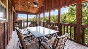Une terrasse extérieure couverte, dotée d’une table et de chaises, de grandes fenêtres et d’un ventilateur de plafond.