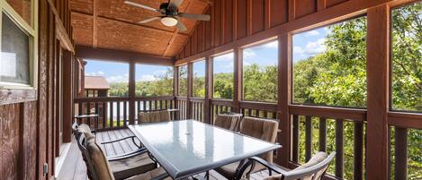 A covered outdoor deck with a table and chairs, large windows, and a ceiling fan.