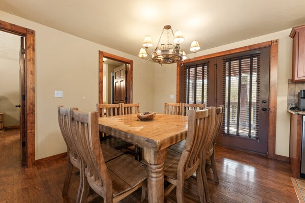 A dining area with a wooden table and chairs, a chandelier, and a door with blinds. - Exquisite Decor in this 6 BD Cabin! Super Close to Fun Attractions and Shops! (Branson West)