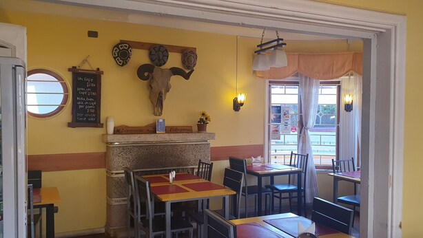 Un interior de restaurante con mesas y sillas, un menú en la pizarra, decoración en la pared y una ventana con vistas.