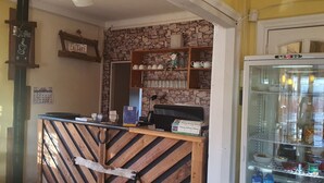 Interior de una cafetería con pared de piedra rústica, mostrador de madera y estanterías con tazas y una máquina de café.