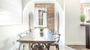 Een eetgedeelte met een lange houten tafel, metalen stoelen en een bakstenen muur met een raam.