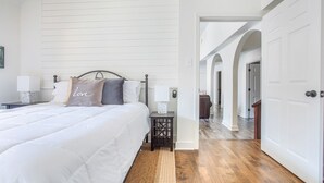 Een slaapkamer met een bed, nachtkastjes en een nachtkastje. Er is een gang die naar een andere kamer leidt.