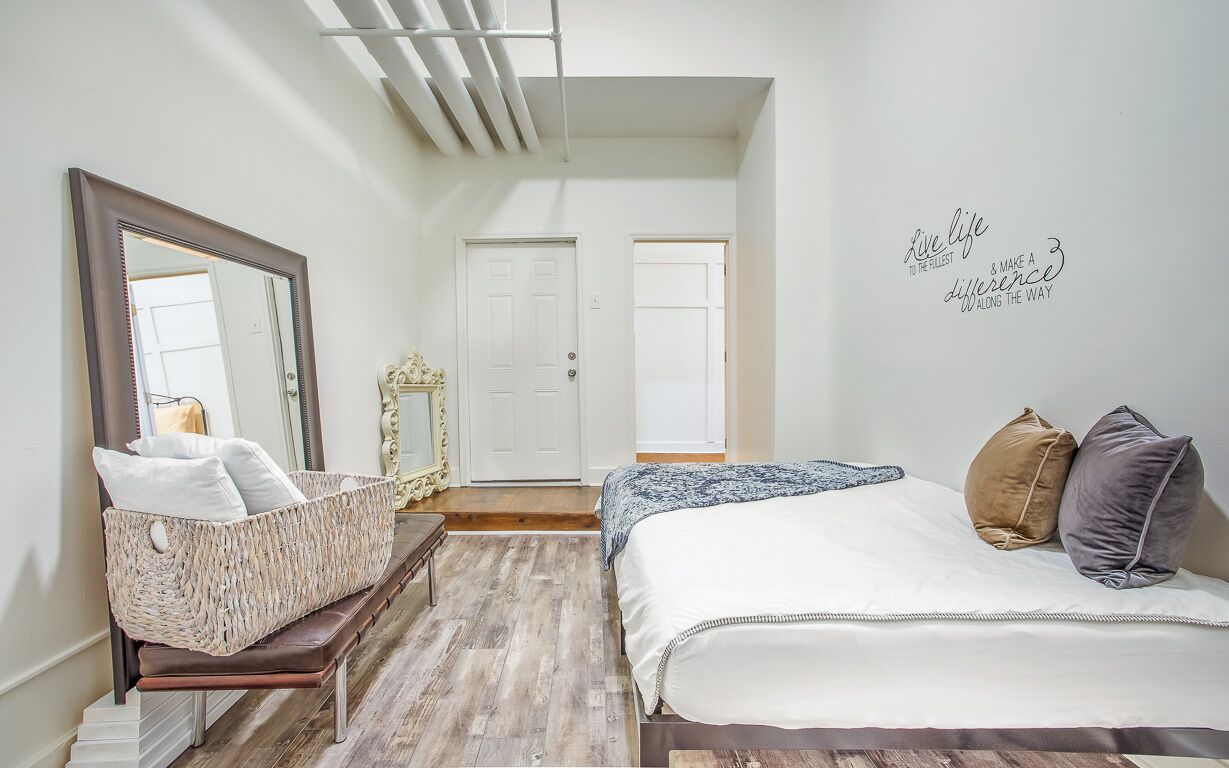 A bedroom with a bed, a mirror, a wicker basket, and a wall with a motivational quote.