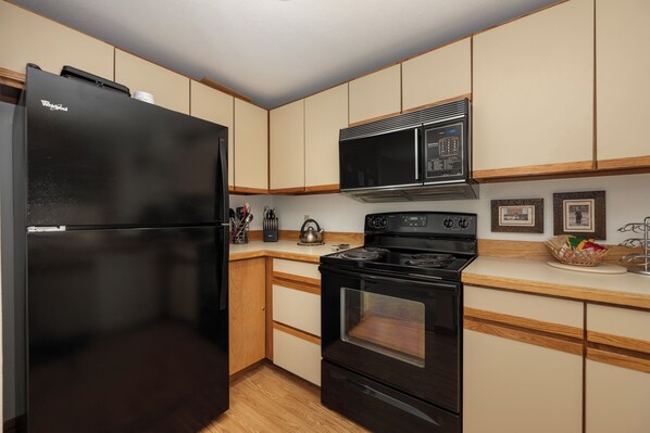 A kitchen with a black refrigerator, a microwave, a stove, and wooden cabinets. - Crestview Place Unit 607 Spacious with mt views & private decks family friendly (Winter Park)