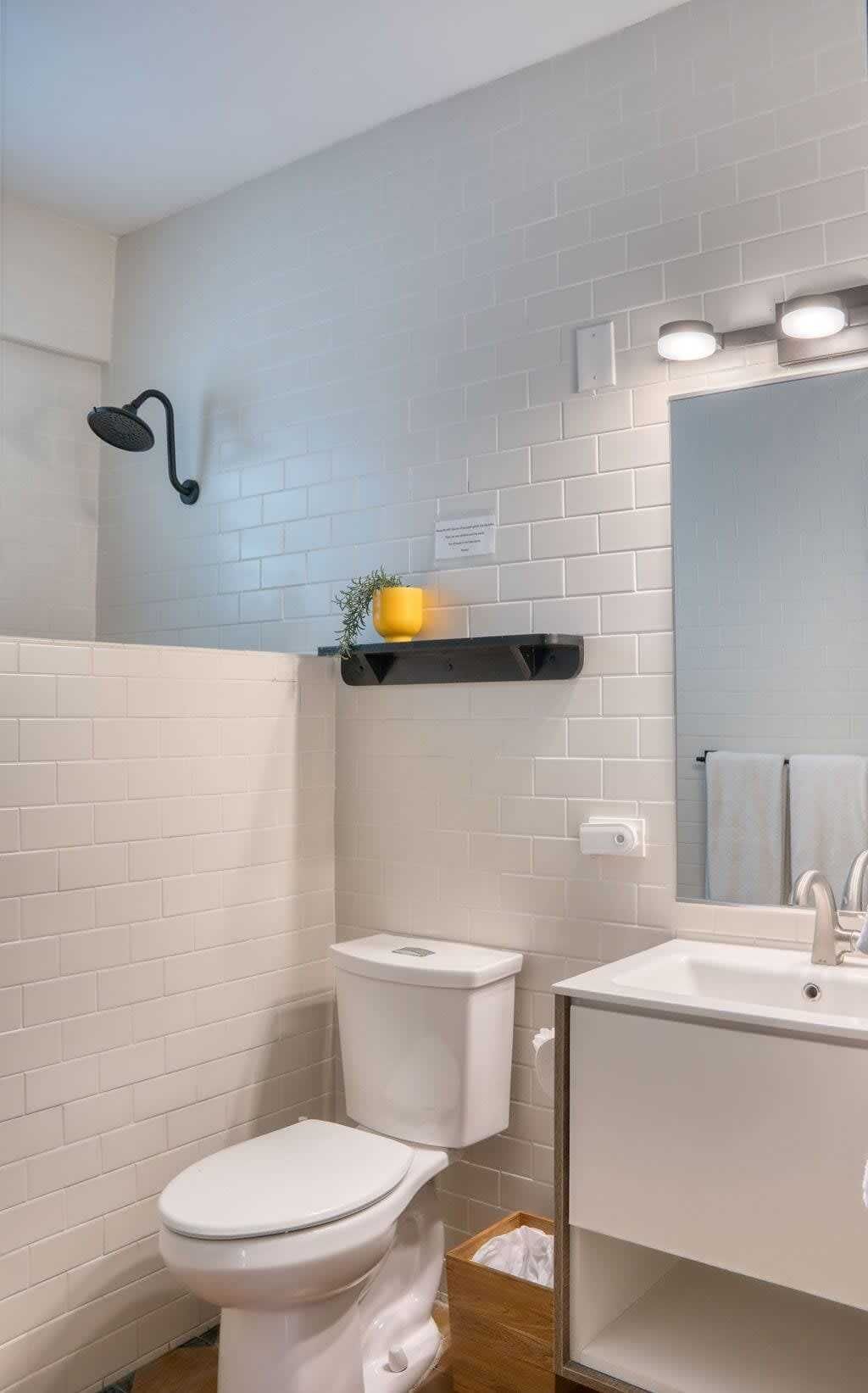 A bathroom with white subway tiles, a white toilet, a sink with a mirror, and a showerhead.