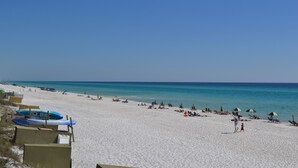 En strand med vit sand, kristallklart blått vatten och flera parasoller.